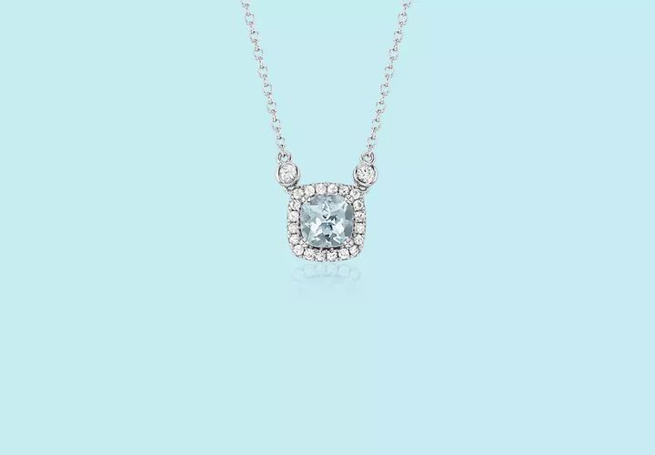 A cushion cut aquamarine gemstone is surrounded by a white sapphire halo on a white gold chain
